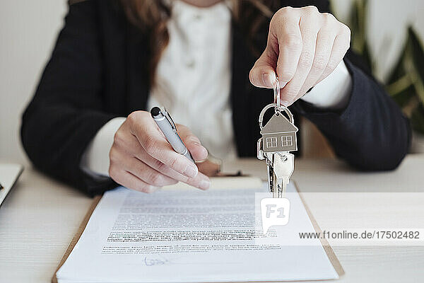 Saleswoman holding house keys and pen at office