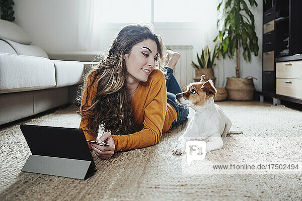 Young woman with tablet PC looking at pet dog lying on floor