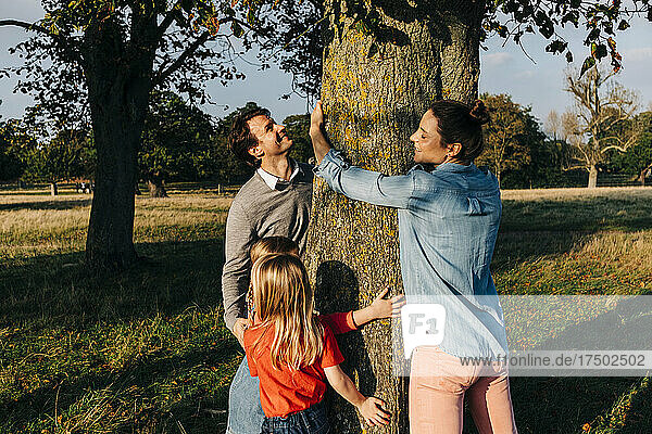 Parents and daughters embracing tree in park on weekend