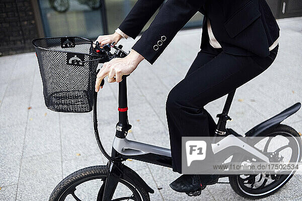 Businesswoman riding electric bicycle with basket on street