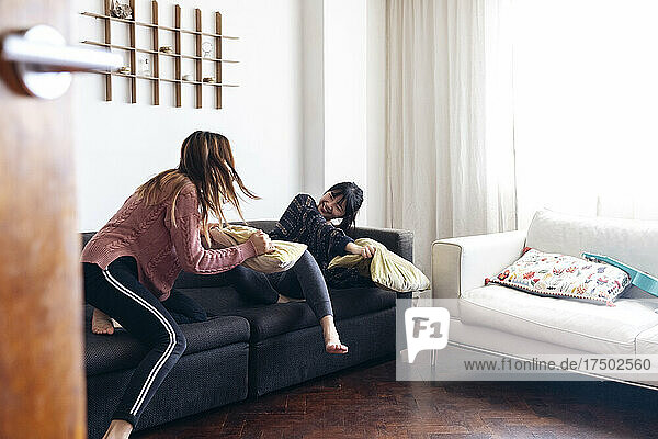 Happy young friends playing with cushions on sofa in living room