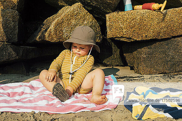 Boy sitting on towel and removing sandal at beach