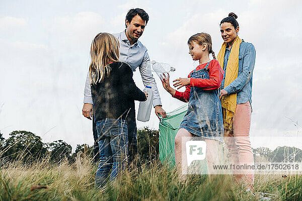 Töchter sammeln mit ihren Eltern Plastikflaschen im Park