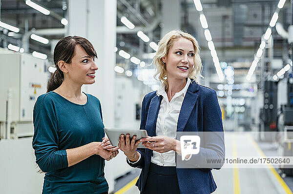 Businesswoman with tablet PC standing by colleague in factory