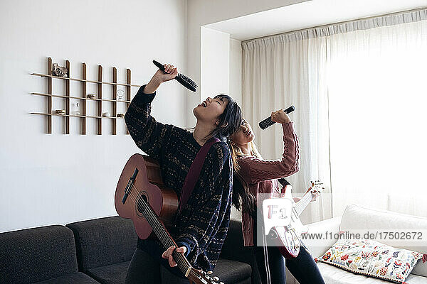 Playful friends holding combs and guitars singing together at home