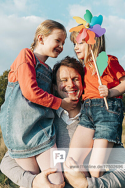 Cheerful father carrying daughters on sunny day