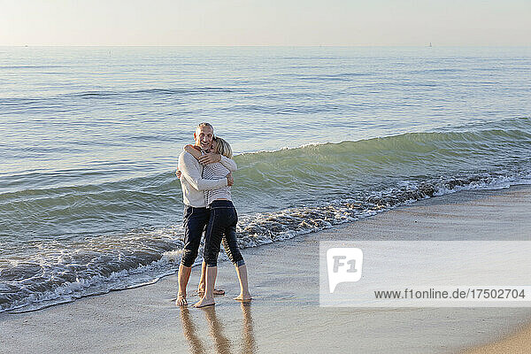 Sorgloses Paar umarmt sich in der Nähe der Küste am Strand