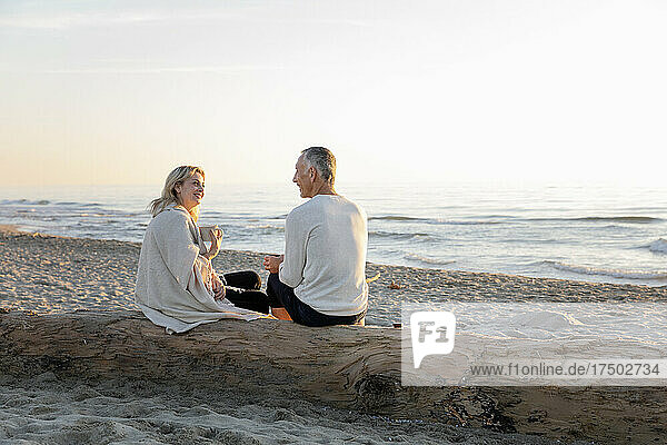 Couple talking to each other sitting on tree log at beach