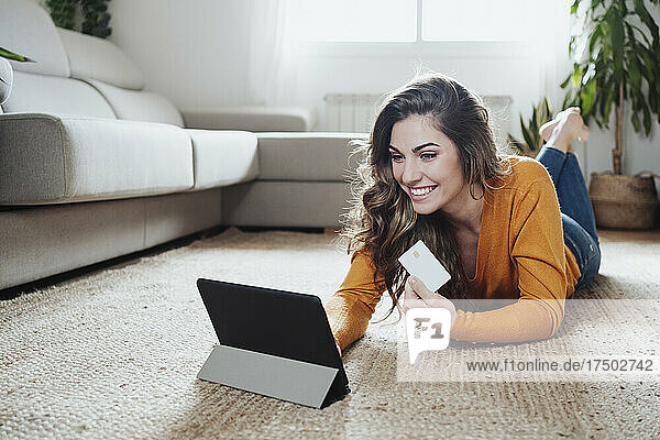 Happy woman doing home shopping through credit card and tablet PC