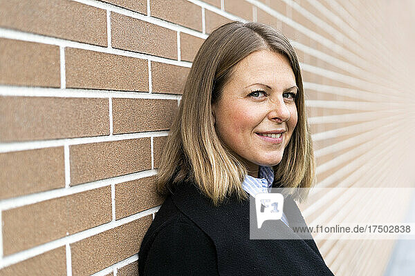 Smiling blond woman leaning on brick wall