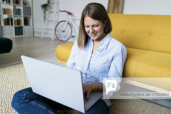 Smiling woman using laptop sitting on carpet at home