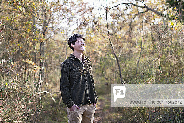 Smiling young man with hands in pockets looking away at forest
