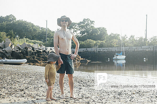 Shirtless man standing with son on sand at beach on vacation