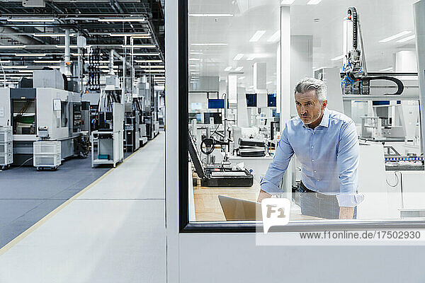 Confident businessman looking through glass at factory