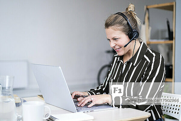 Businesswoman with headphones using laptop at home office