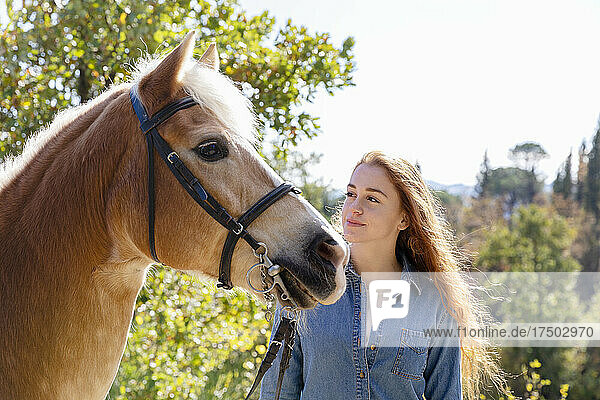 Junge Frau steht an einem sonnigen Tag neben dem Pferd