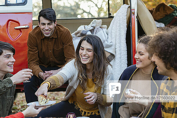 Cheerful woman serving cake to friends outside van on picnic