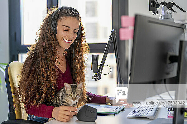 Lächelnde junge Frau blickt auf die Katze auf dem Schreibtisch