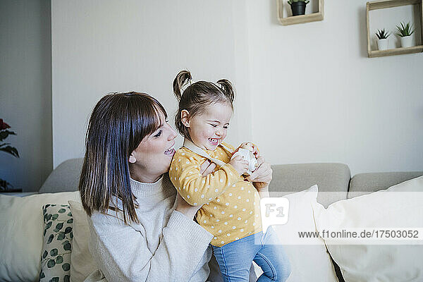 Smiling mother holding playful daughter on sofa