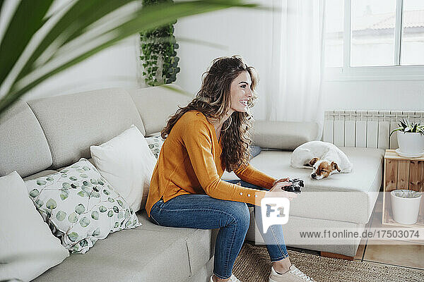 Woman sitting on sofa playing video game at home