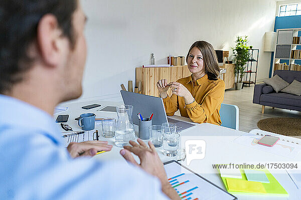 Smiling businesswoman looking at colleague gesturing at office