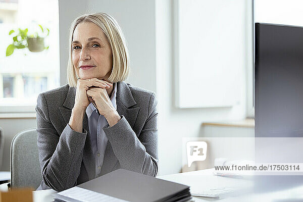 Blond businesswoman with hands on chin at desk