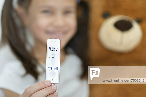 Smiling girl with teddy bear showing rapid diagnostic test result