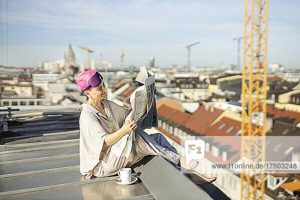 Lächelnde Frau sitzt auf dem Dach und liest Zeitung