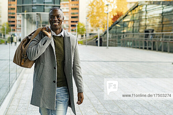 Smiling businessman with duffel bag walking on footpath