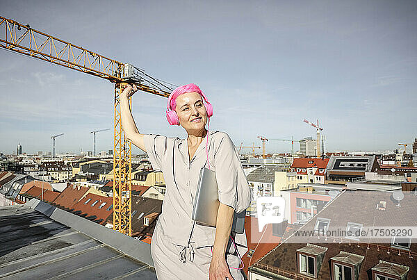 Woman with laptop listening music through headphones on rooftop
