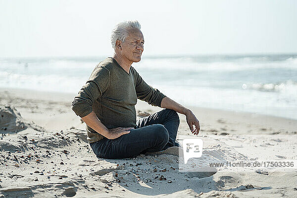 Smiling senior man sitting cross-legged on sand at beach
