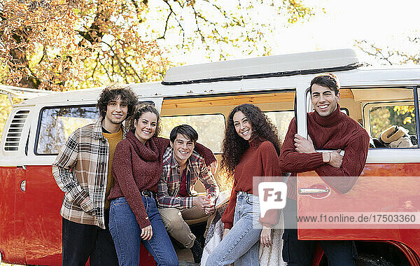 Happy friends at motor home in autumn forest on weekend