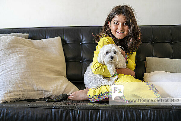 Smiling girl sitting with dog on sofa at home