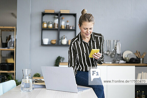 Freelancer with laptop using mobile phone at table
