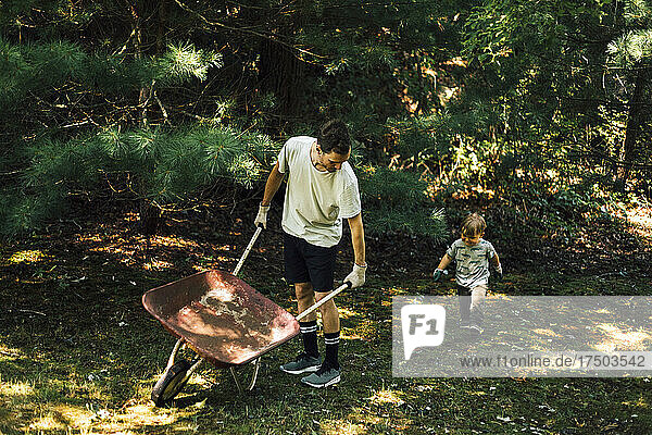 Son walking behind father with wheelbarrow