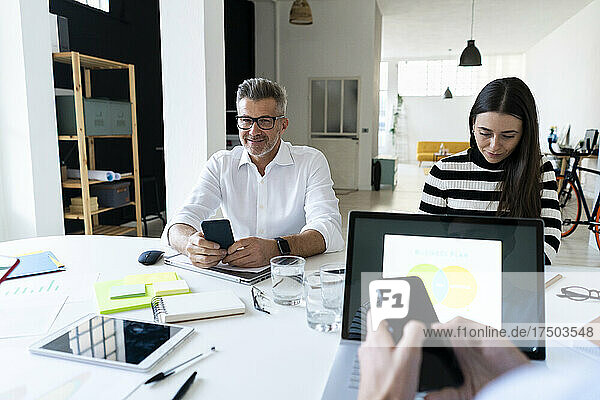 Businessman with smart phone sitting with colleagues working at office