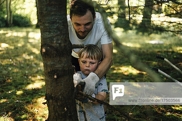 Man assisting son cutting branch of tree