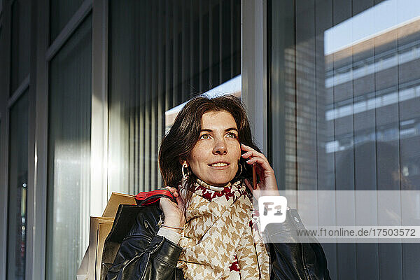 Woman with shopping bags talking on mobile phone at corridor