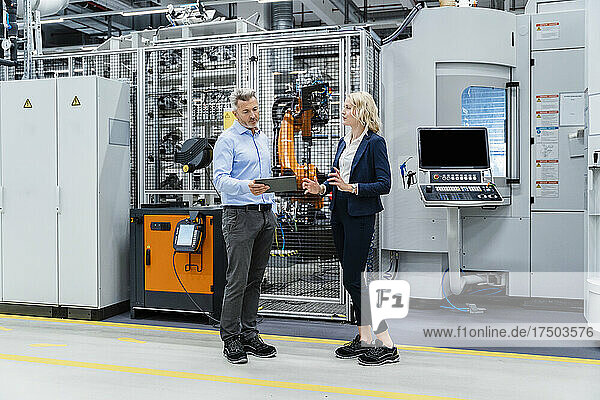 Businesswoman discussing with coworker holding tablet PC in factory