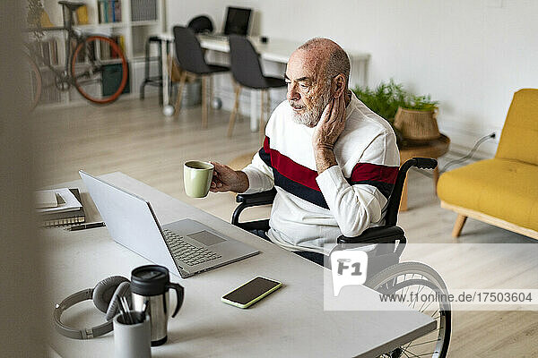 Businessman holding coffee cup on wheelchair at desk