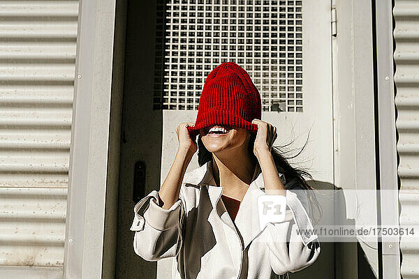 Woman hiding face with knit hat in front of door