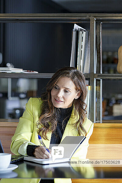 Businesswoman writing in diary at table in cafe