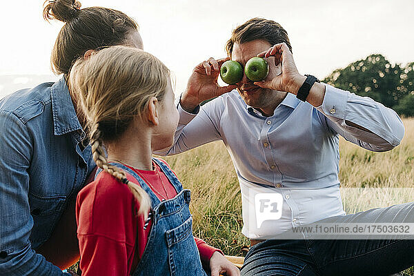 Father covering eyes with fruits while playing with daughter at park