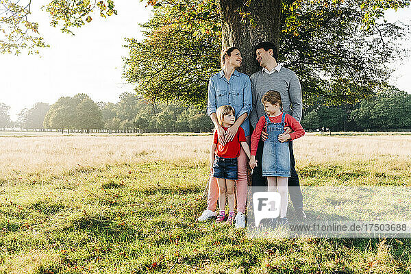 Smiling parents with daughter standing in front of tree on sunny day