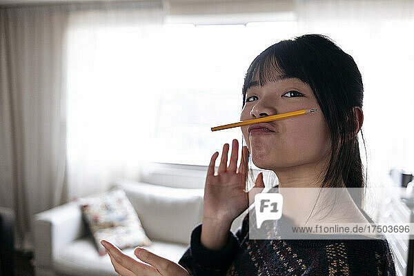 Young woman holding pencil on puckered lips at home