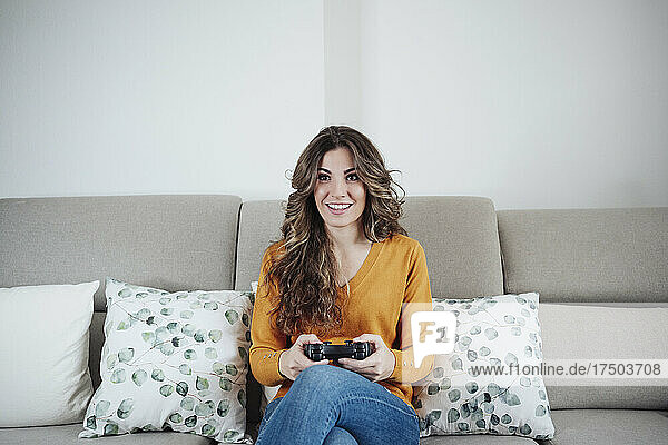 Frau mit Joystick spielt Videospiel und sitzt zu Hause auf dem Sofa