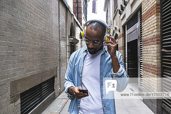 Man with headphones using smart phone walking in alley