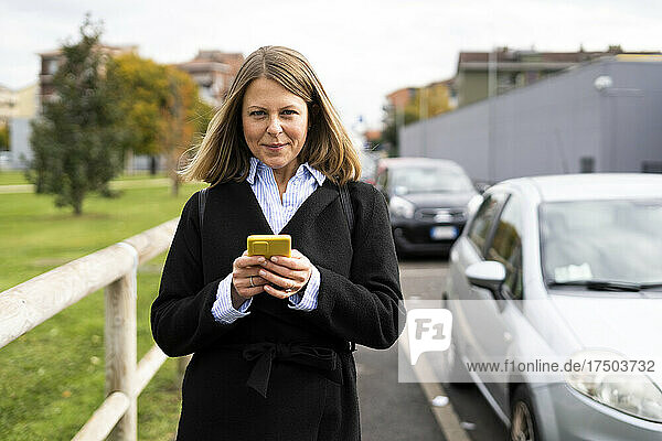 Woman wearing jacket holding mobile phone on road