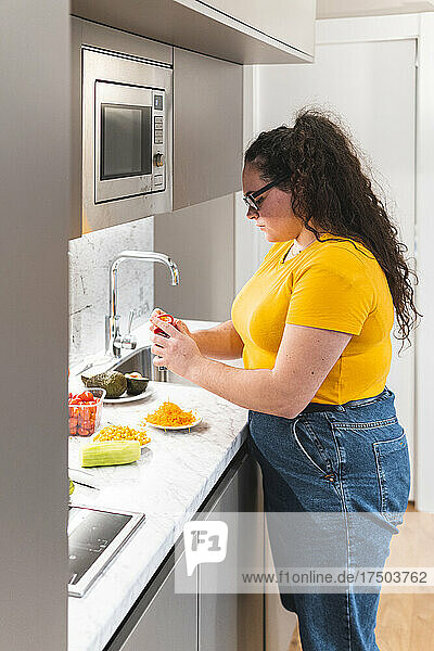Young woman grating cheese standing in kitchen at home