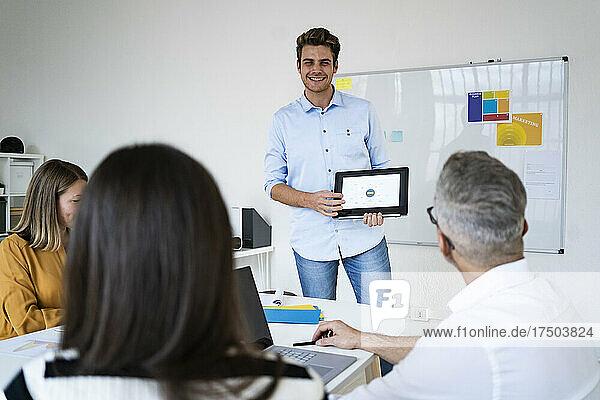 Young businessman showing presentation to colleagues on tablet PC at office